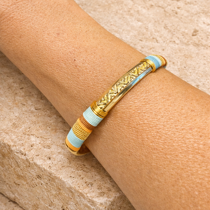 Gold and light blue bracelet on a wrist against a beige stone background