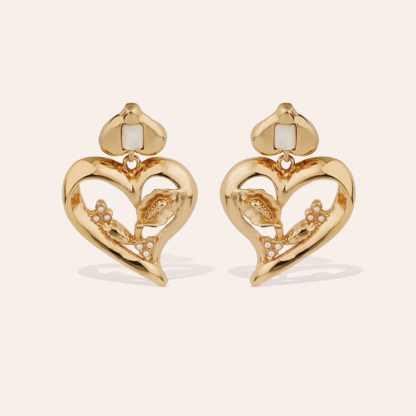 Gold love heart statement earrings with mother of pearl stones intertwined on cream background