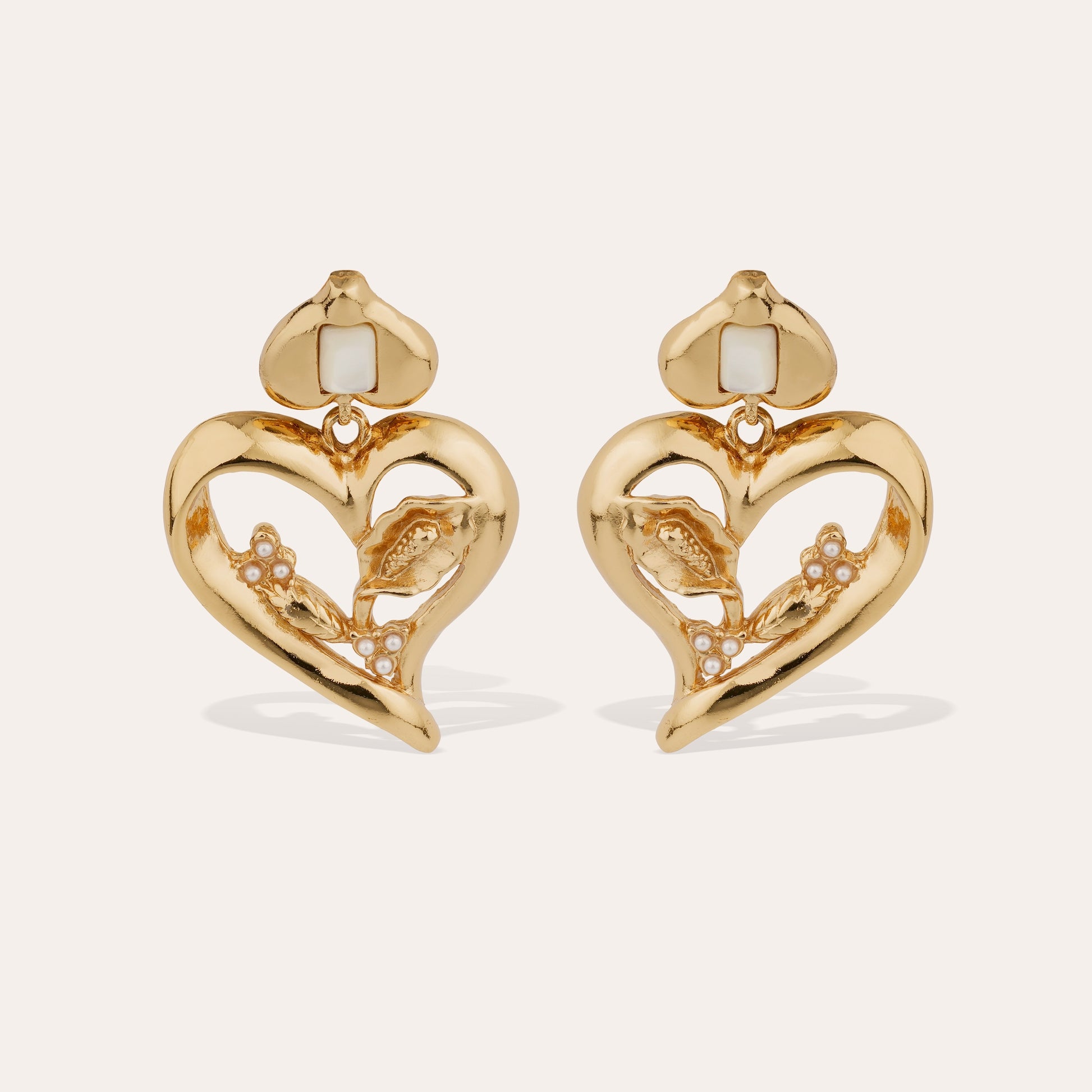 Gold love heart statement earrings with mother of pearl stones intertwined on cream background