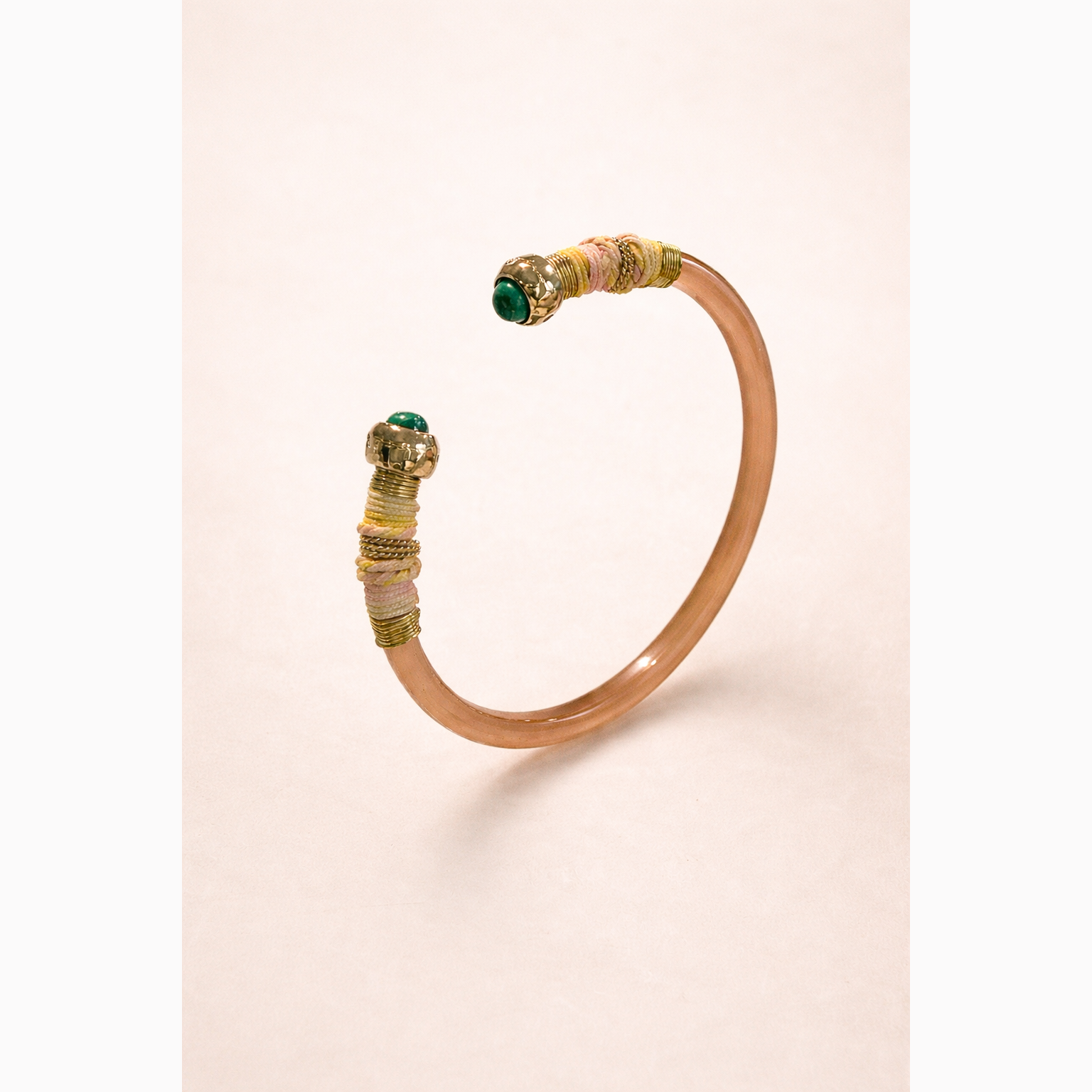 Decorative bangle with gold and green accents on a beige background
