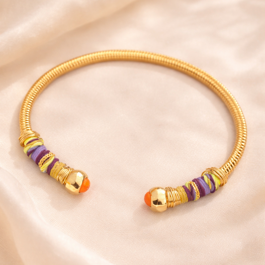 Gold Bangle with purple threads and orange beads on the end on soft linen background