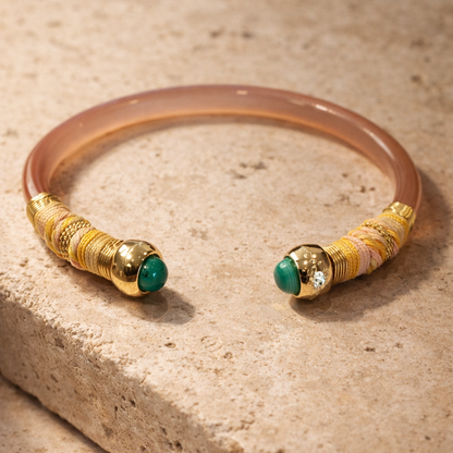 Bracelet with gold and green beads on a beige stone surface