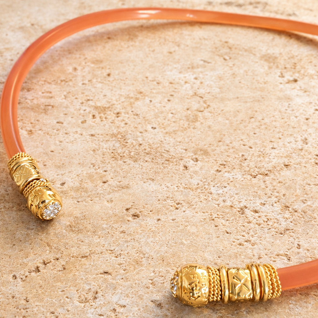Pink acetate choker necklace with stone and gold ends on travertine base.