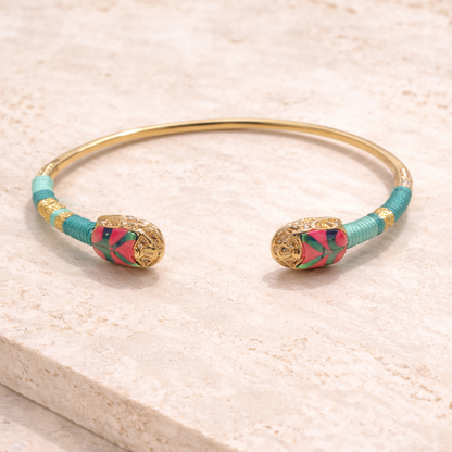 Gold bangle with turquoise and pink design on a light travertine surface