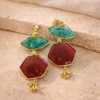 Pair of earrings with green and red gemstones on a beige fabric background