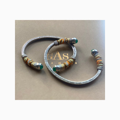 two silver bangles on a gas bijoux gift box, each have green stones at the ends and wrapped partially with coloured threads
