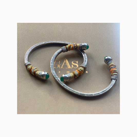 two silver bangles on a gas bijoux gift box, each have green stones at the ends and wrapped partially with coloured threads