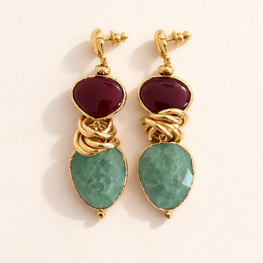 Gold earrings with red and green gemstones on a beige background