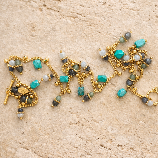Necklace with gold chain, turquoise, and gray beads on a beige stone surface