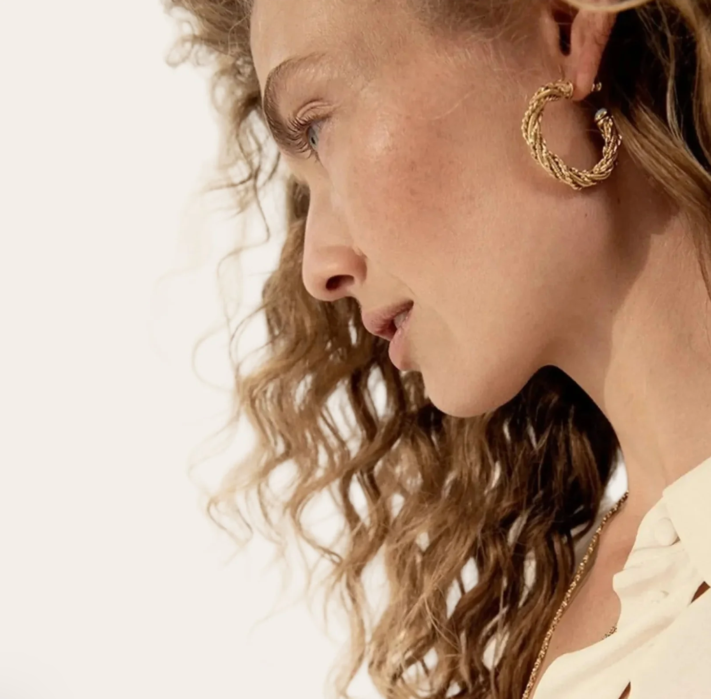 Close-up of a person wearing gold hoop earrings with a neutral background