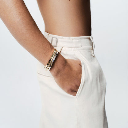 Silver and gold mesh bangle on a mans arm, wearing white pants and white background