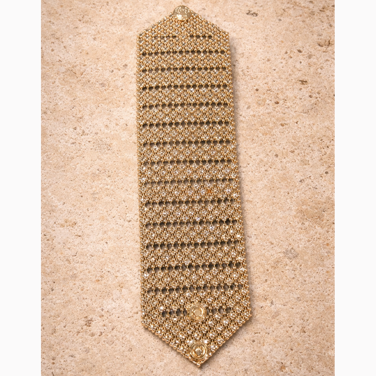 Gold bracelet stretched out on a beige textured background