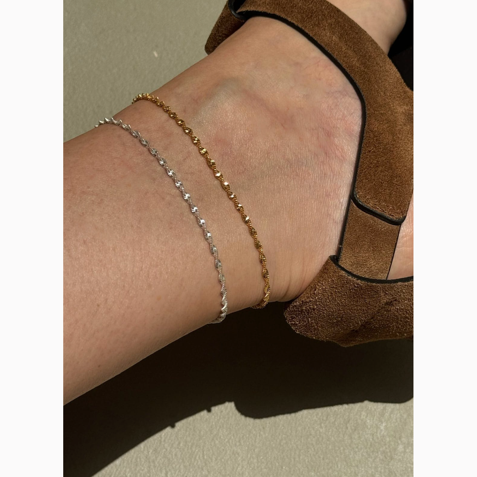 Close-up of a foot wearing a brown sandal with a gold anklet on a neutral background