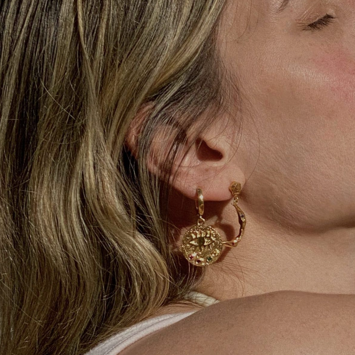 Close-up of a person wearing gold hoop earrings with a neutral background