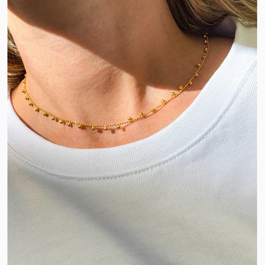 Gold necklace worn by a person on a white background
