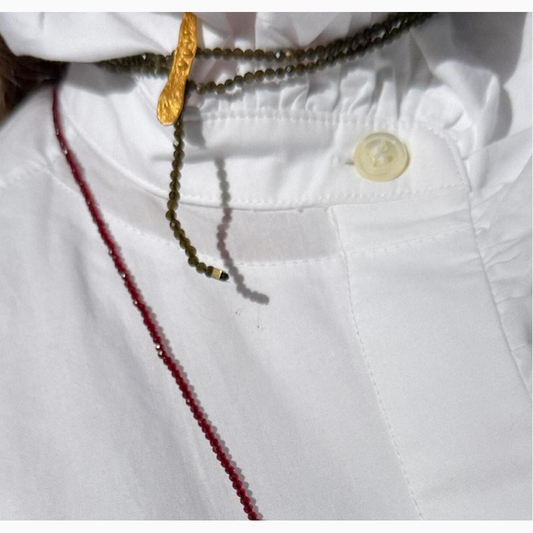 Close-up of a white garment with red stitching, gold button, and beaded necklace.
