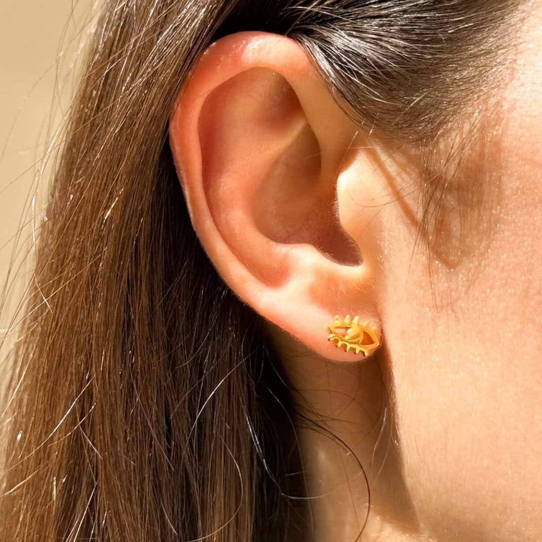 Close-up of an ear wearing a gold earring with an eye design.