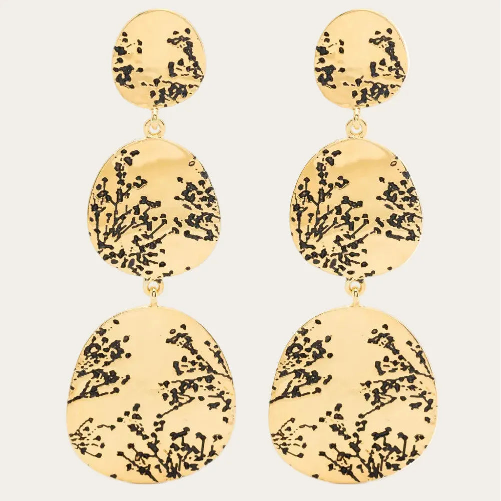 Gold earrings with black floral patterns on a white background
