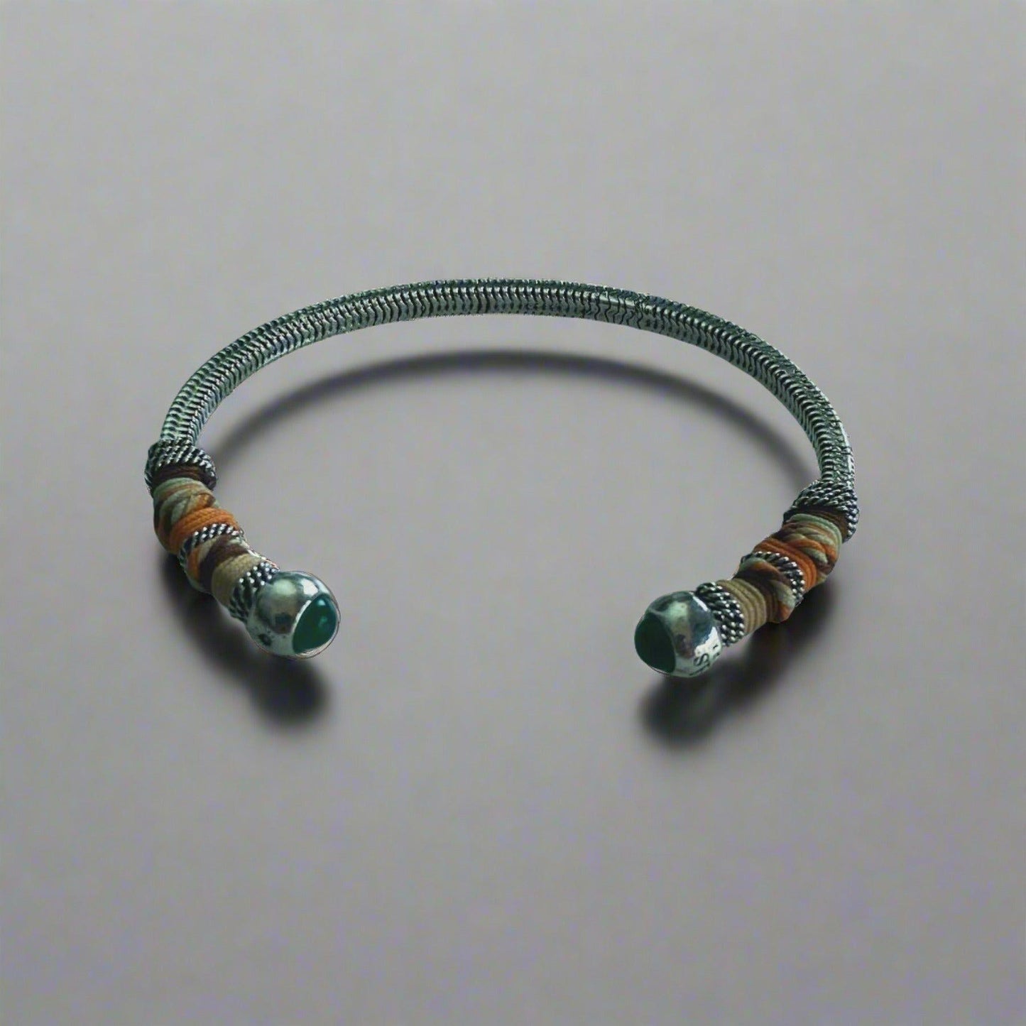 silver bangle with green stone bead ends,wrapped in colourful threads on neutral background