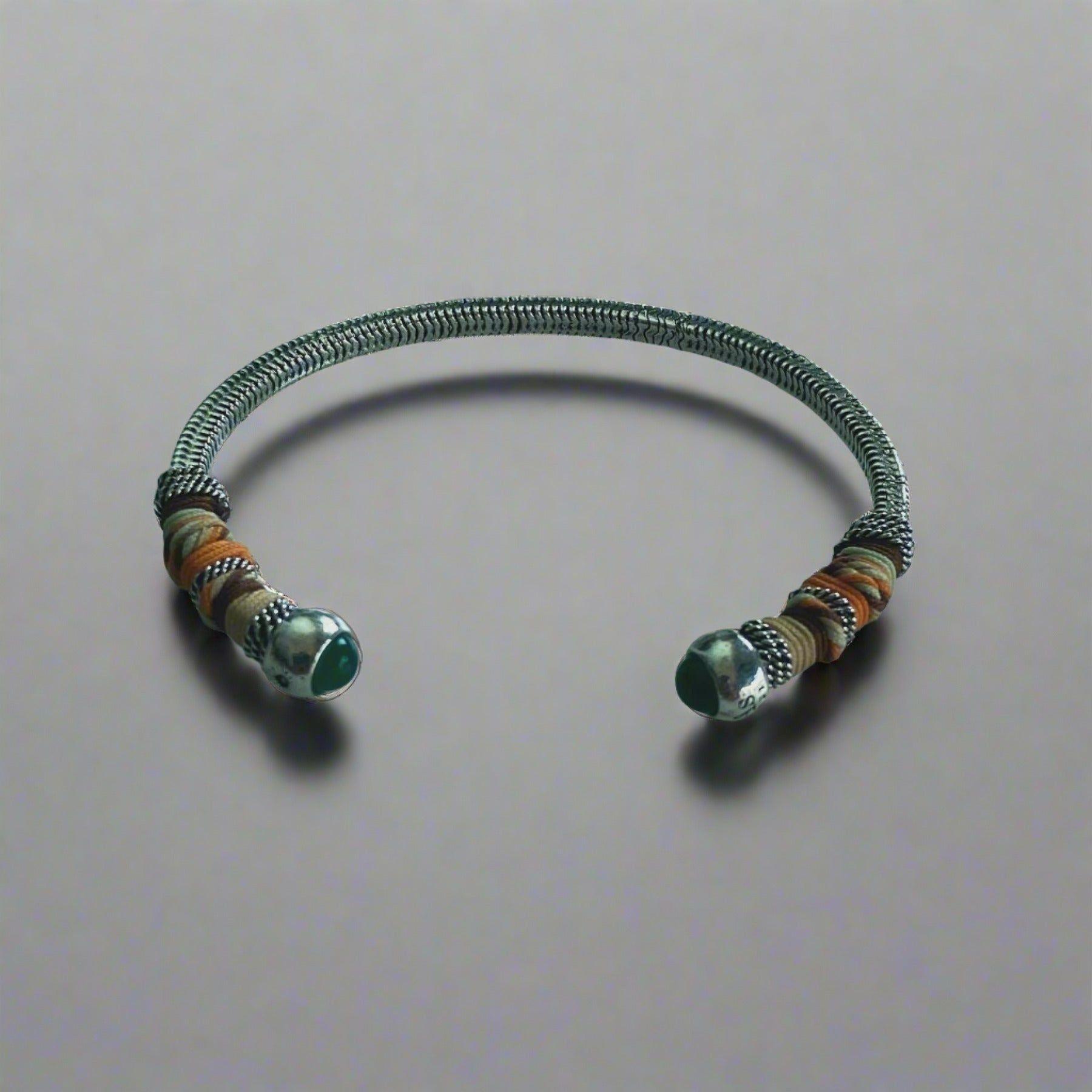 silver bangle with green stone bead ends,wrapped in colourful threads on neutral background