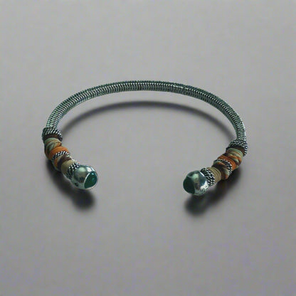 silver bangle with green stone bead ends,wrapped in colourful threads on neutral background
