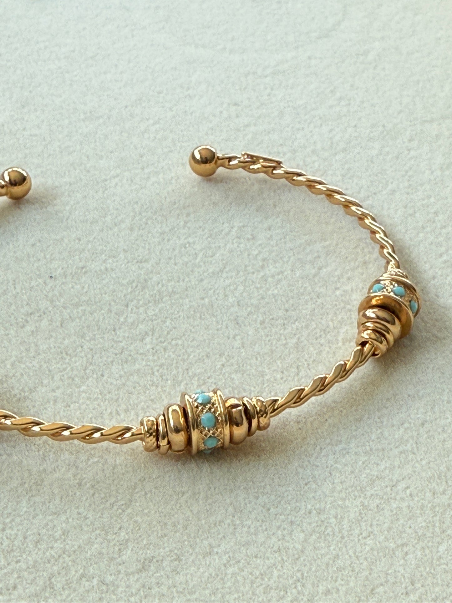 Gold bracelet with turquoise stones on a light gray background