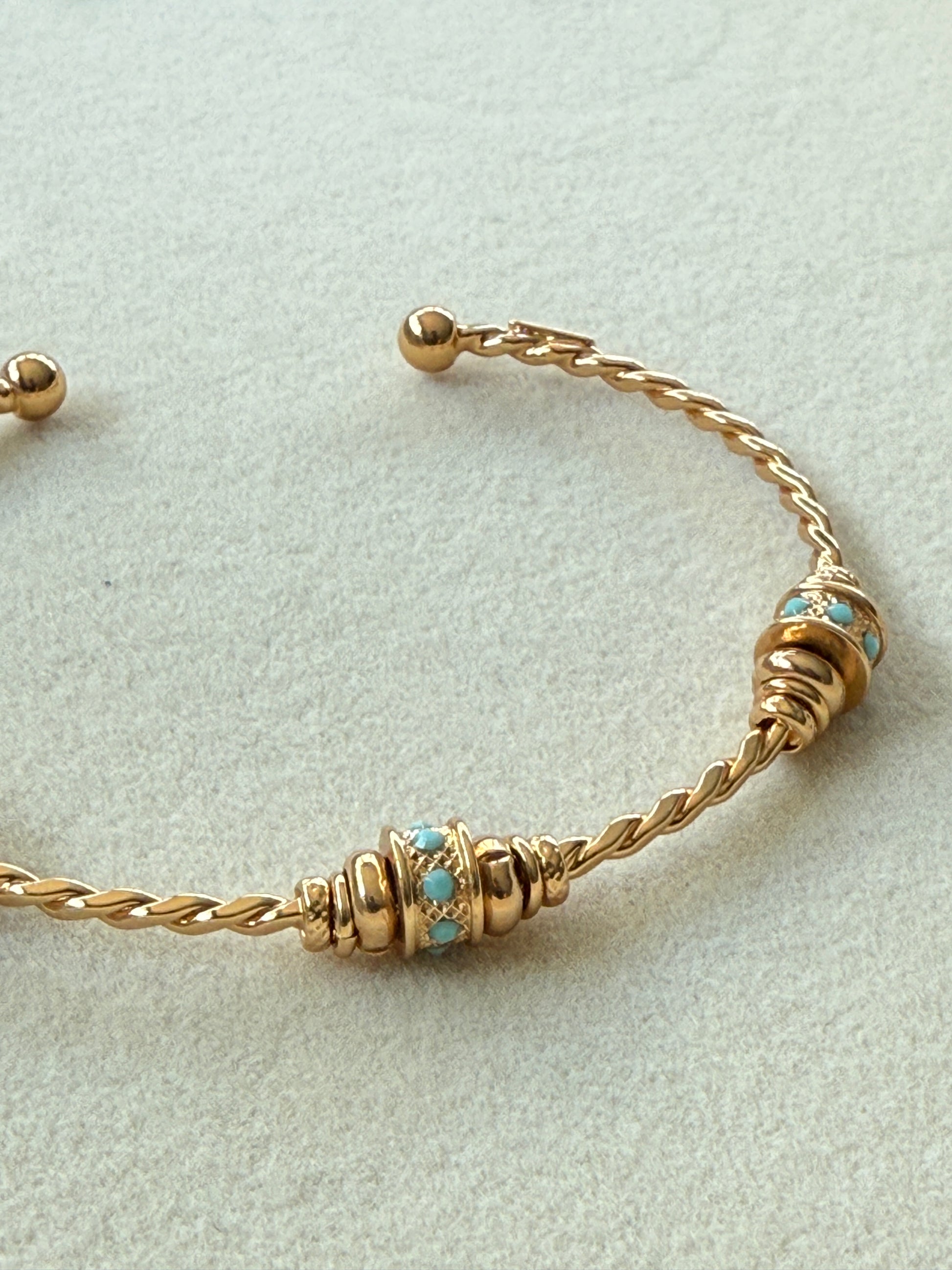 Gold bracelet with turquoise stones on a light gray background