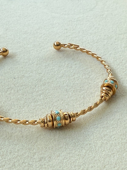 Gold bracelet with turquoise stones on a light gray background