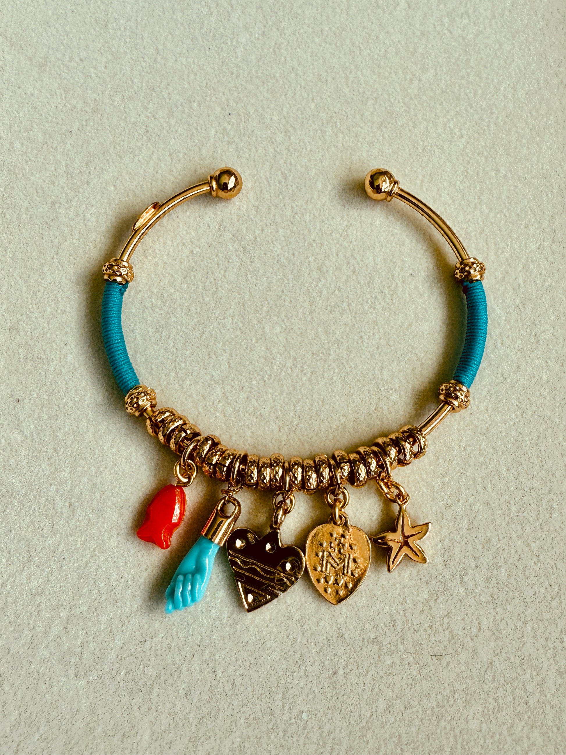 Bracelet with turquoise bead and gold charms on a light gray background