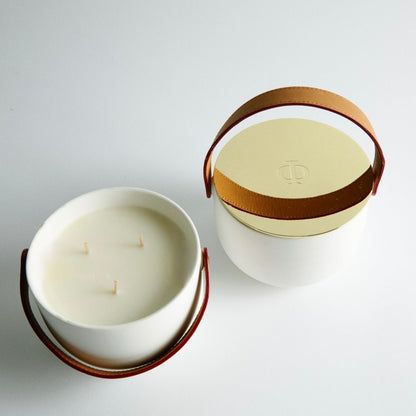 Two candles in white containers with brown handles on a light gray background