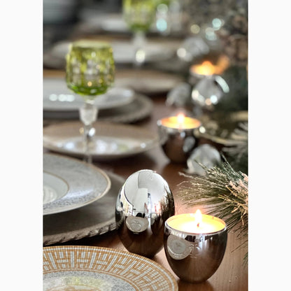 Elegant silver egg-shaped candle holders with a candle inside, and decorative flowers in the background.