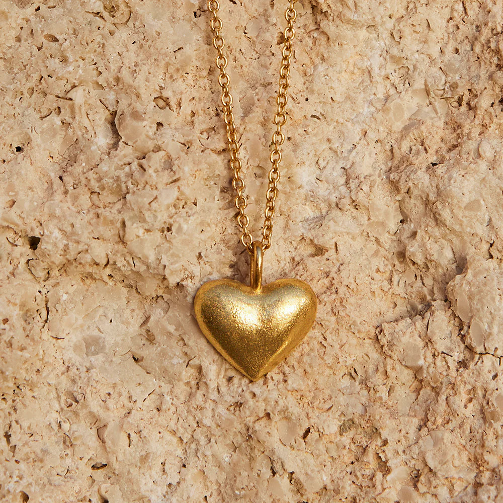Gold heart-shaped pendant necklace on a beige stone surface