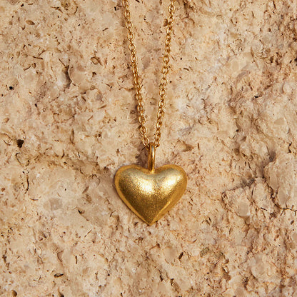 Gold heart-shaped pendant necklace on a beige stone surface