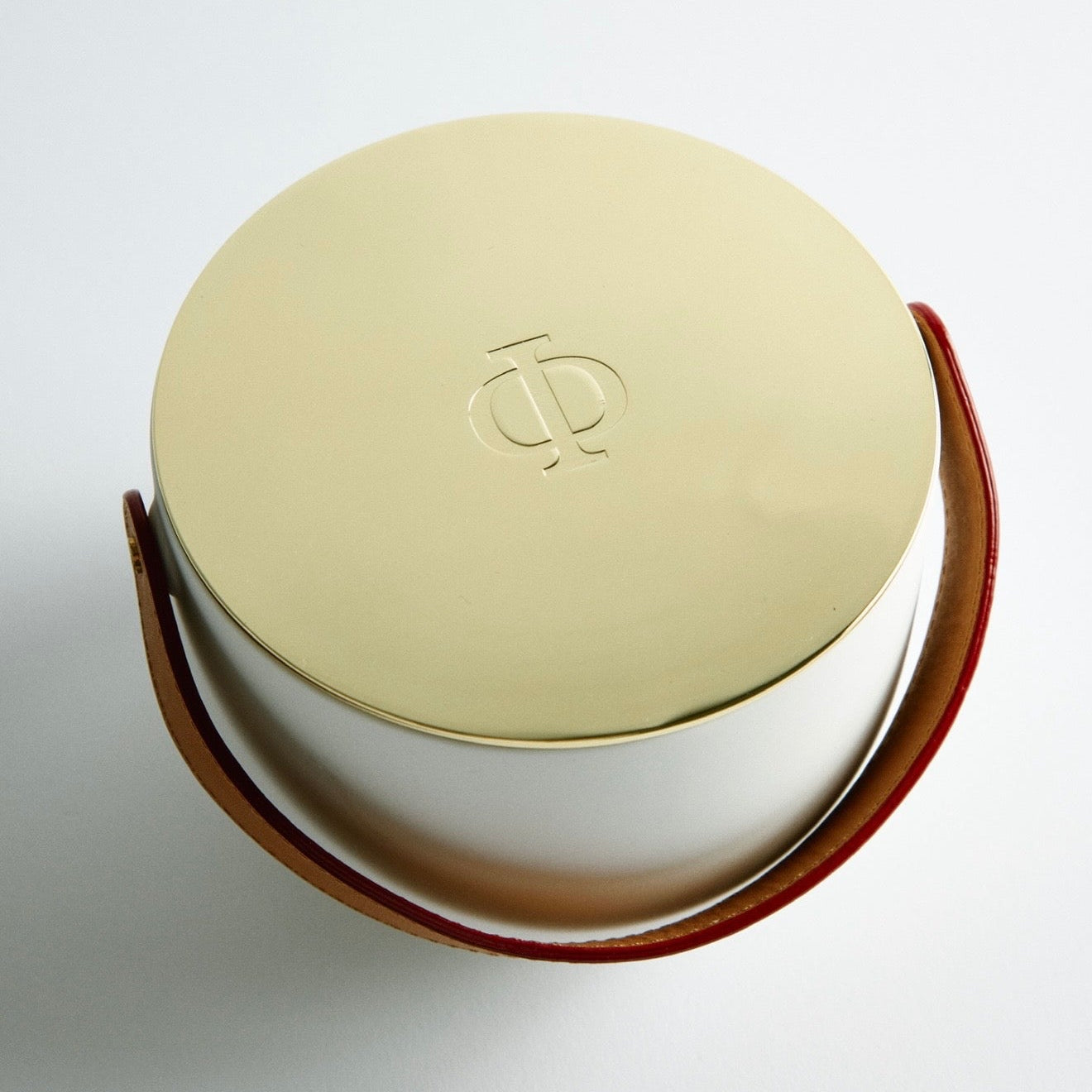 Ceramic candle with a gold lid and brown leather strap on a light gray background