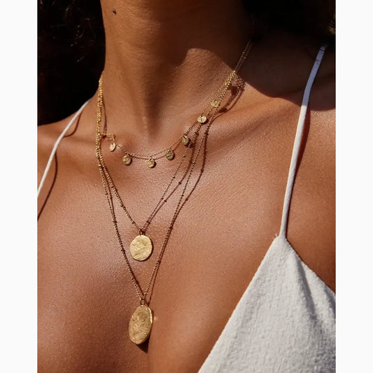 Close-up of a person wearing gold necklaces with a neutral background