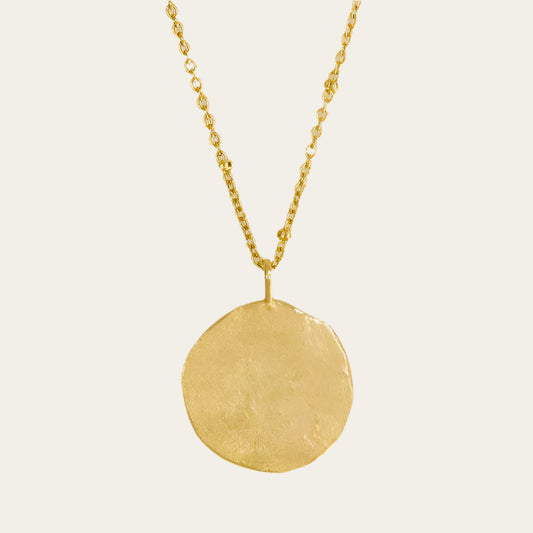 A gold-plated hammered full moon pendant necklace displayed on a mannequin.