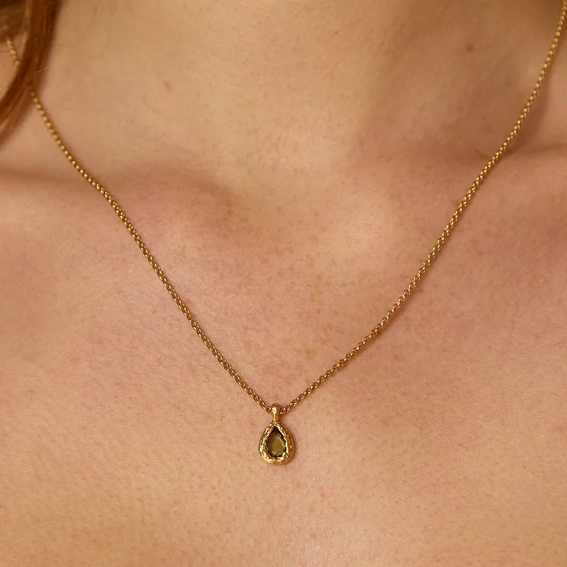Gold necklace with a green teardrop pendant on a person's neck