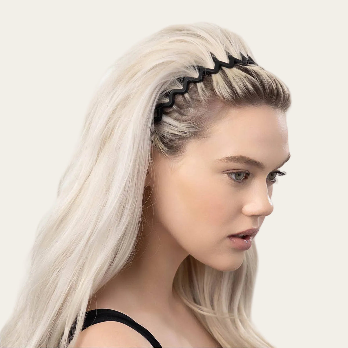Woman with blonde hair styled in a side part, wearing a black headband against a light gray background