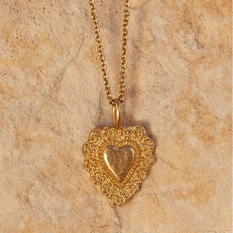 Gold heart-shaped pendant necklace on a beige stone surface