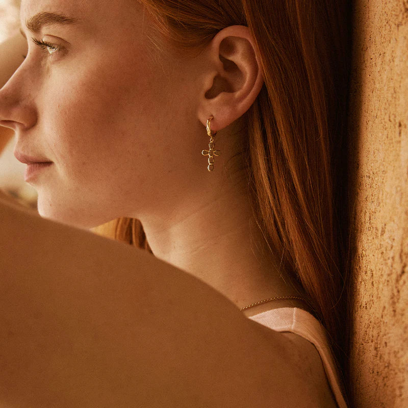Close-up of a woman wearing gold earrings against a warm-toned background
