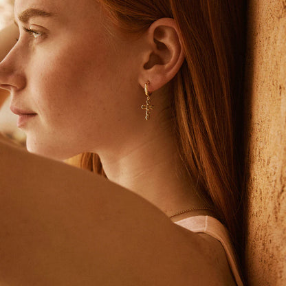 Close-up of a woman wearing gold earrings against a warm-toned background