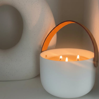 Ceramic candle lit with leather handle on shelf 