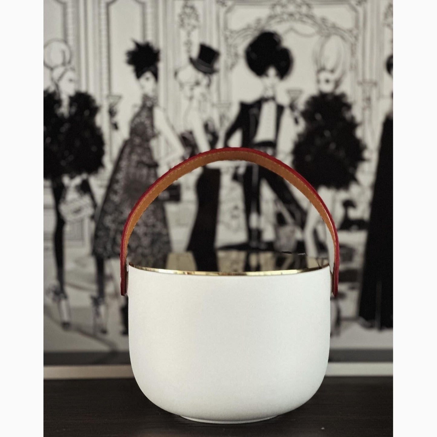 A white ceramic candle with a gold-plated lid and a brown leather handle, displayed against a black and white background.
