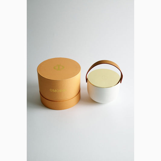 White ceramic container with a brown handle next to an open gold lid on a white background
