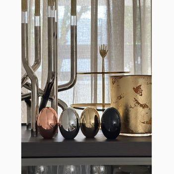 rose gold, silver, gold, black Omorfi egg candles on shelf with decorative decor in background