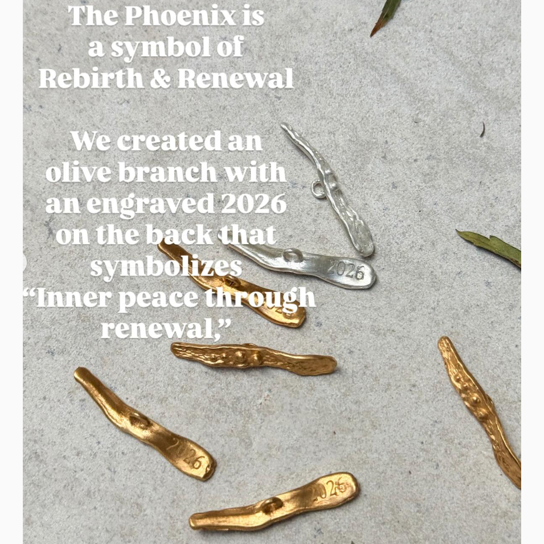 Gold and silver olive branch pendants with engraved '2026' on a textured surface.