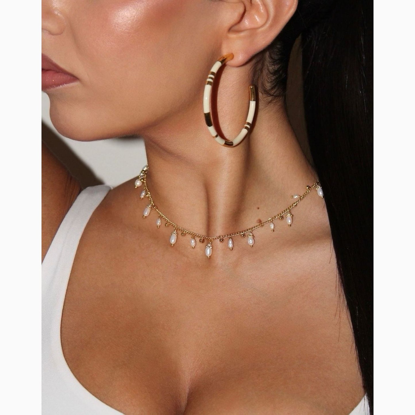 Close-up of a person wearing gold hoop earrings and a delicate necklace with small beads.