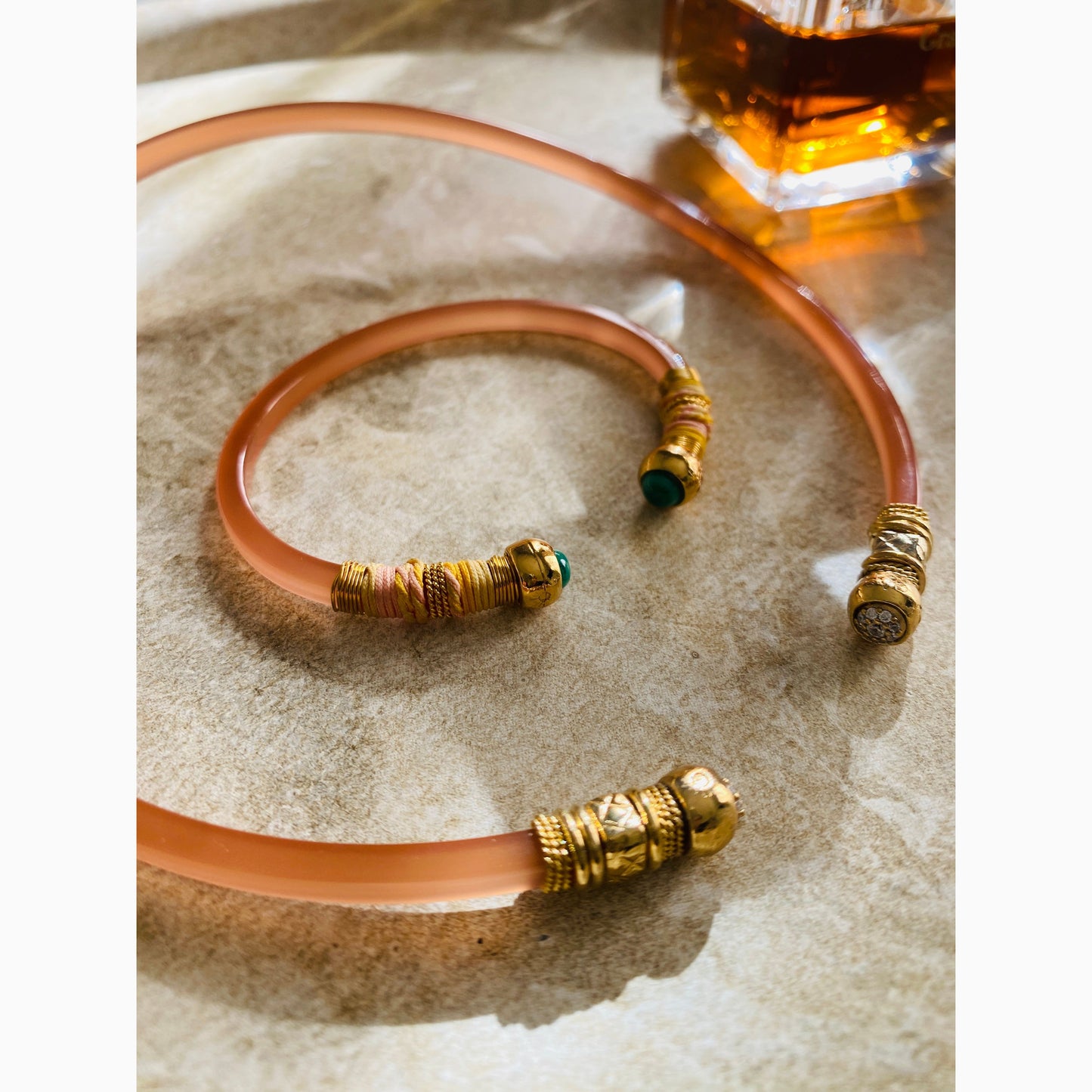 A gold-colored choker necklace with wrapped wires and beads, displayed on a textured surface with matching bracelet