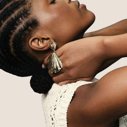 Woman wearing a white crochet top against a blue background and silver shell drop earrings