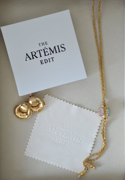 Gold necklace and earrings on a white jewellery cloth with 'The Artemis Edit' branding.